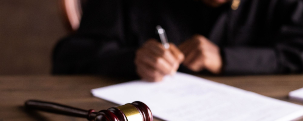 Image of judge writing on a piece of paper with a gavel in the foreground