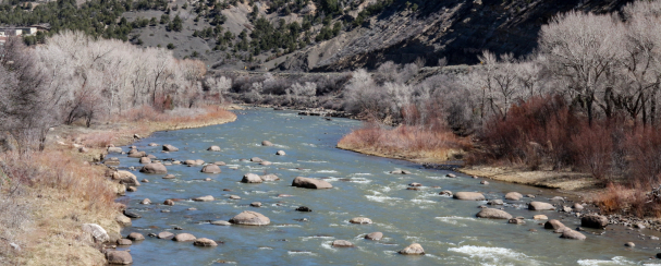 Curvy stream of water with large rocks exposed with a hillside in the background.