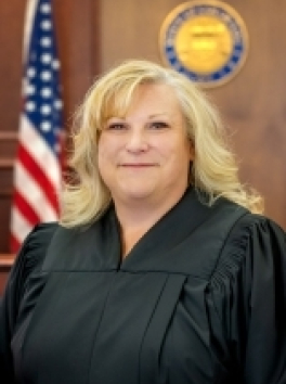 Color photo of Judge Shay Whitaker with robe, seal and flag
