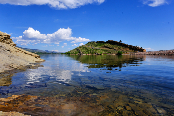 A view across the surface of Horsetooth Reservoir with a bright blue sky and white clouds
